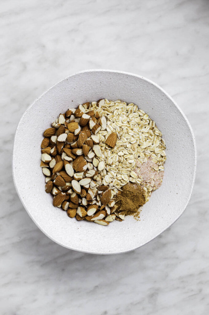 Oats, almonds and spices added in a white bowl.