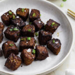 Air fryer tempeh in a white plate, topped with green onion and flaky sea salt.