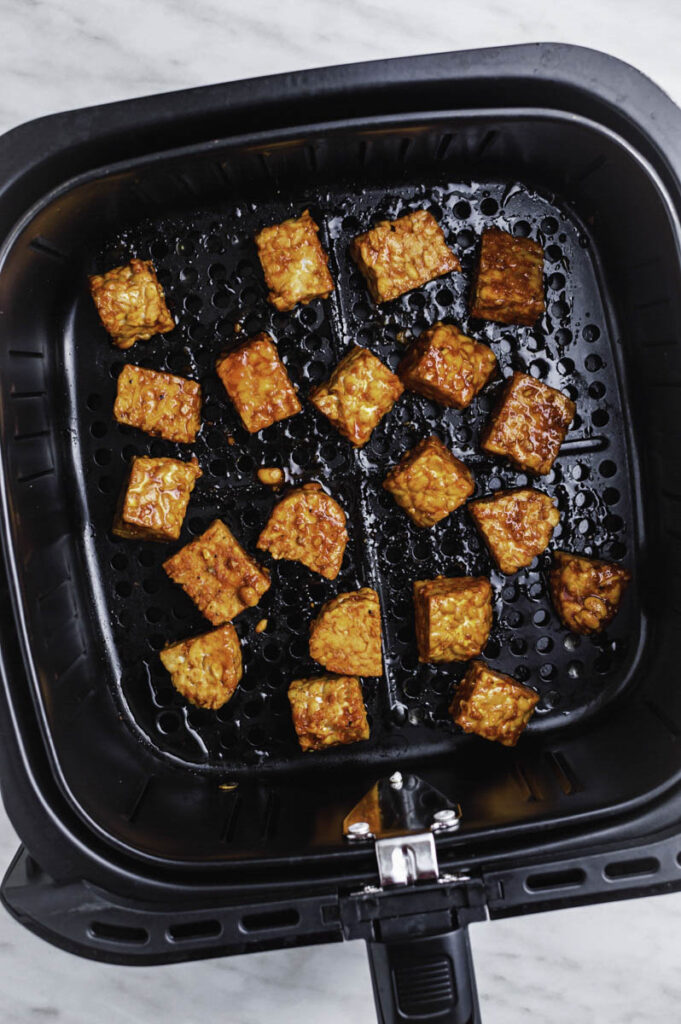 Marinated tempeh pieces in an air fryer basket.