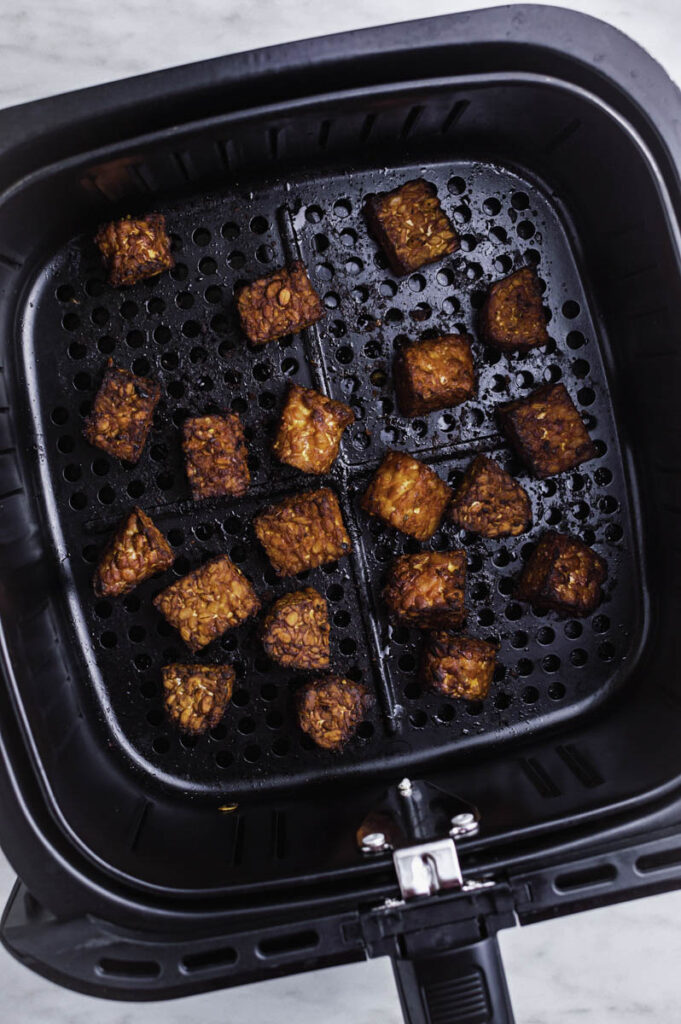 Crispy tempeh pieces in an air fryer basket.
