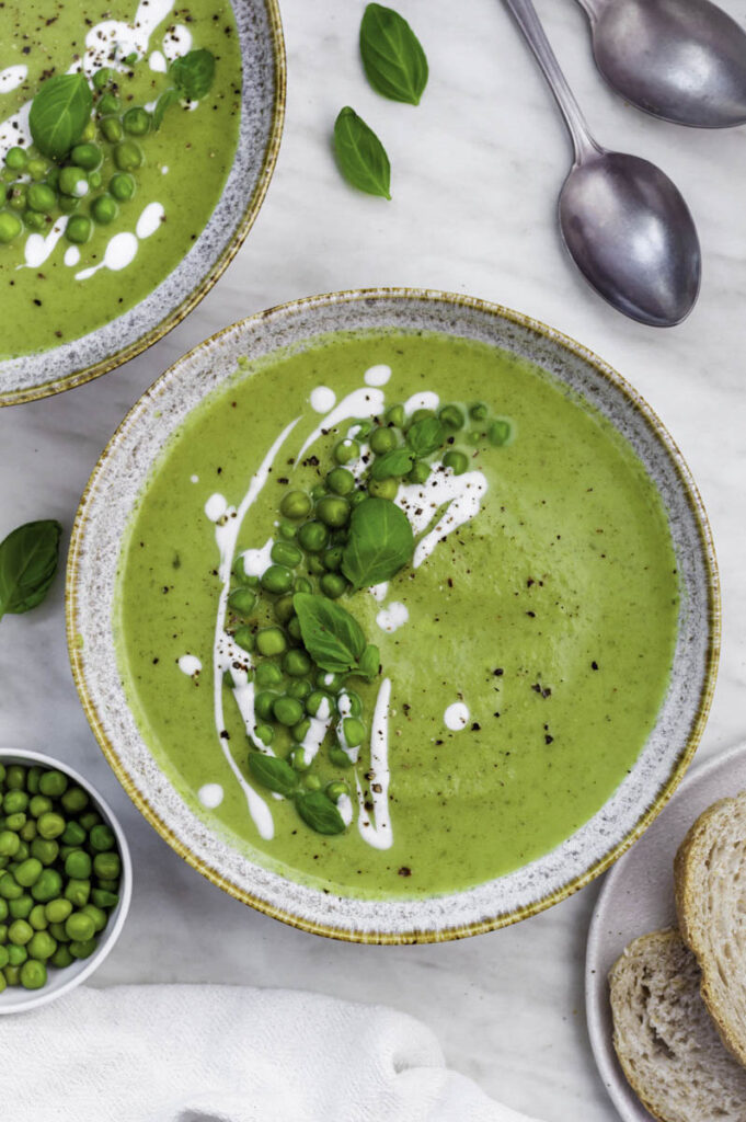 Broccoli pea soup served in a blue bowl, topped with peas, coconut milk, and fresh basil leaves.