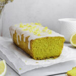 Lemon turmeric tea cake on a white plate, topped with powdered sugar glaze and lemon zest.