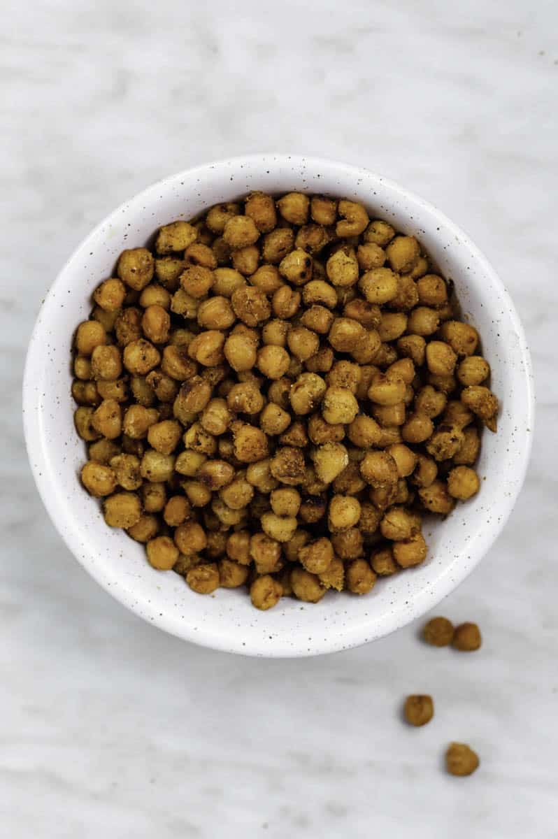 Fried chickpeas in a white bowl,  placed on a white marble background.