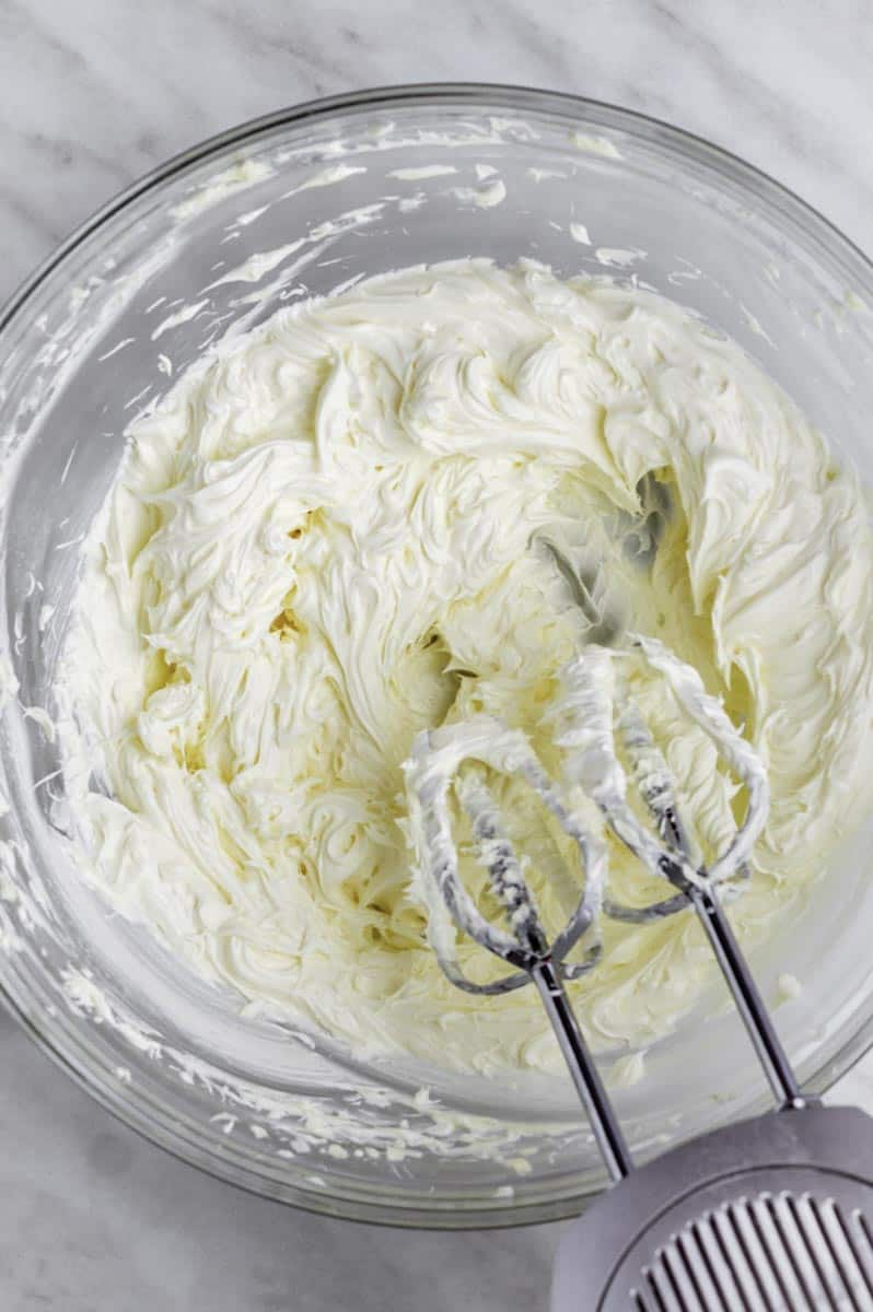 Beating butter in a clear bowl with an electric handheld mixer.