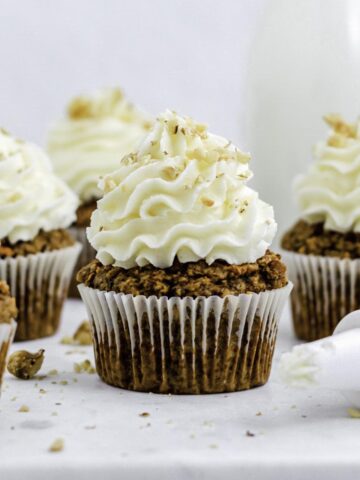 Five carrot cake cupcakes on a marble platter, topped with carrot cake frosting without cream cheese.