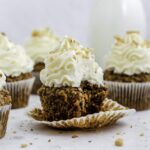 Five carrot cake cupcakes on a marble platter. On one of them was taken a bite out of it.