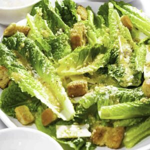 Caesar salad with romaine lettuce, croutons, and homemade dressing served in a white plate.