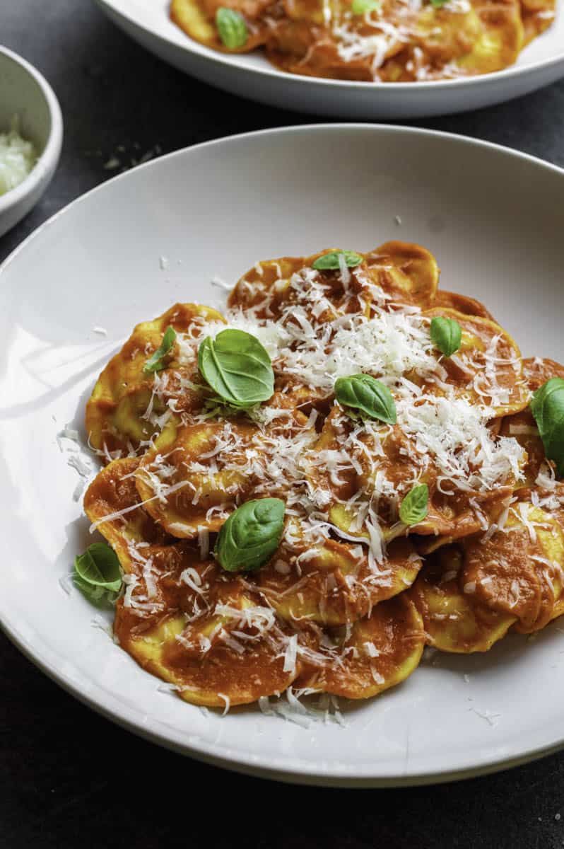 Ravioli Pomodoro served in a white plate and topped with grated parmesan cheese and basil.