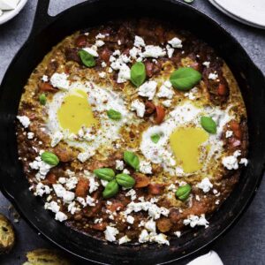 Shakshuka for one served from a cast-iron skillet and topped with feta cheese, basil leaves and red pepper flakes.