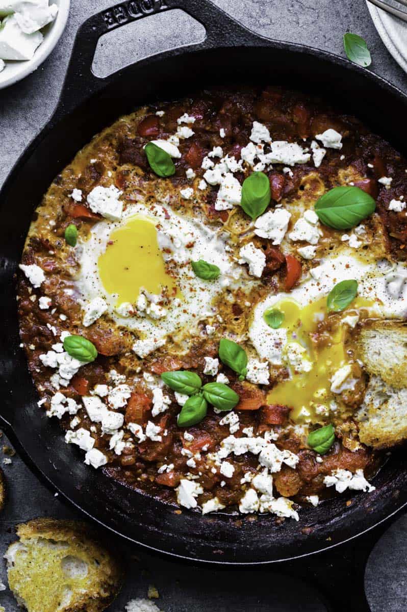 Close-up photo of shakshuka with runny egg yolks in a cast-iron skillet.