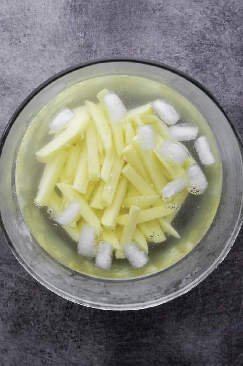 Sliced potatoes soaking in a large bowl filled with water and ice.