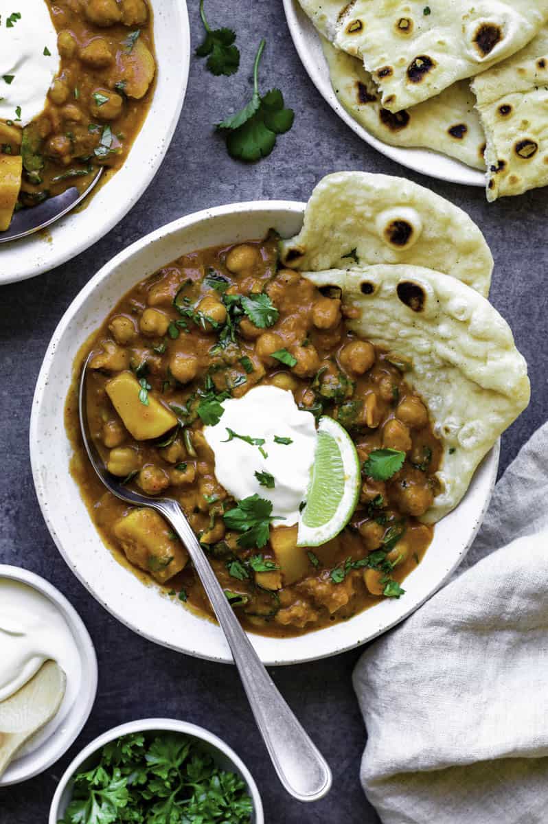 Our garam masala curry recipe served in a white bowl with naan, topped with sour cream, chopped cilantro and a wedge of lime.