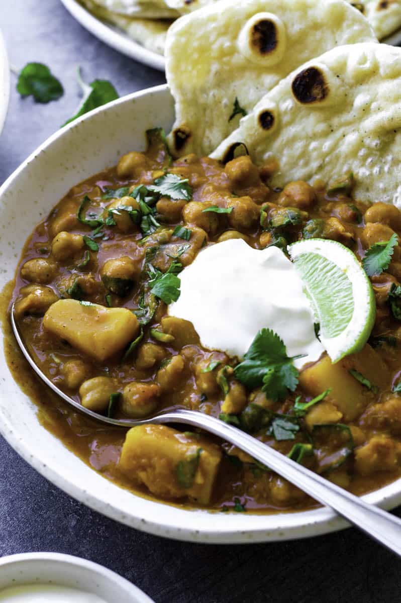 A white bowl filled with garam masala curry with a silver spoon in it. The curry is topped with sour cream and fresh cilantro.