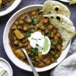 Our garam masala curry recipe served in a white bowl with naan, topped with sour cream, chopped cilantro and a wedge of lime.