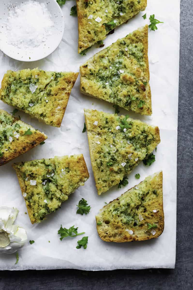 A few pieces of ciabatta garlic bread placed on a piece of parchment paper and topped with flaky salt and fresh parsley.