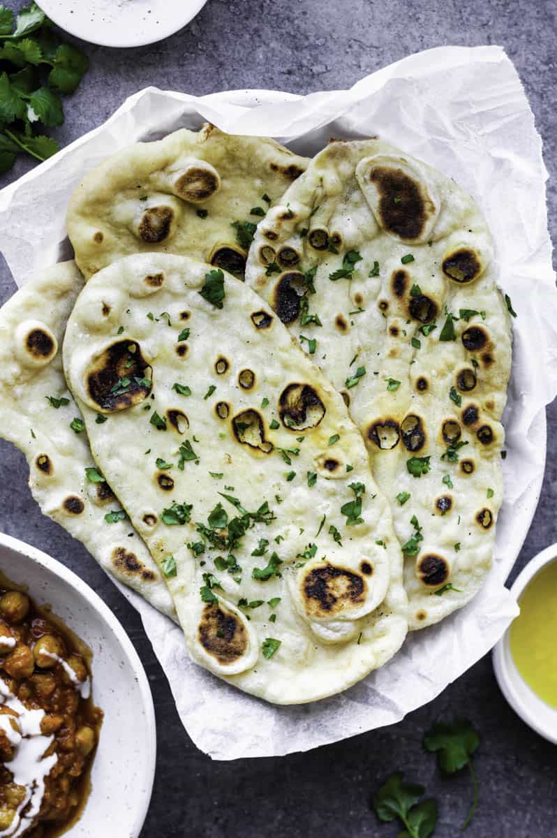 A few pieces of naan bread without yogurt served in a white bowl layered with parchment paper, topped with chopped cilantro.