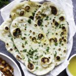A few pieces of naan bread without yogurt served in a white bowl layered with parchment paper, topped with chopped cilantro.