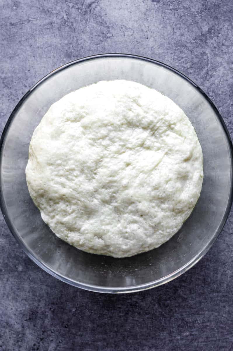 Risen naan dough in a mixing bowl.