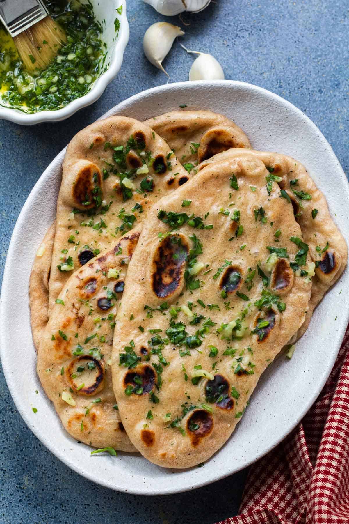 Whole wheat garlic naan piled up on a white plate. A small bowl of garlic butter next to it.