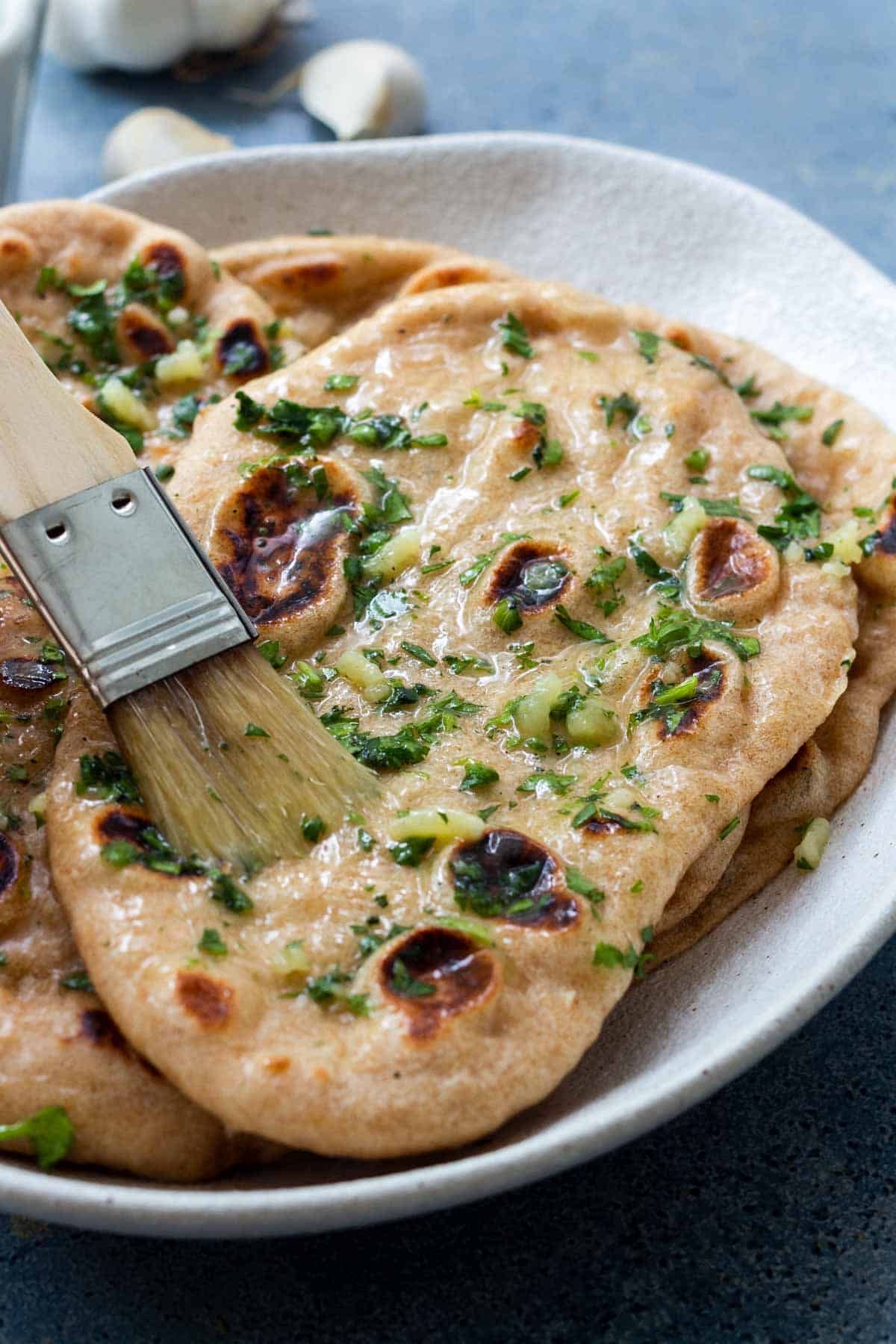 Brushing naan with garlic butter using a pastry brush.