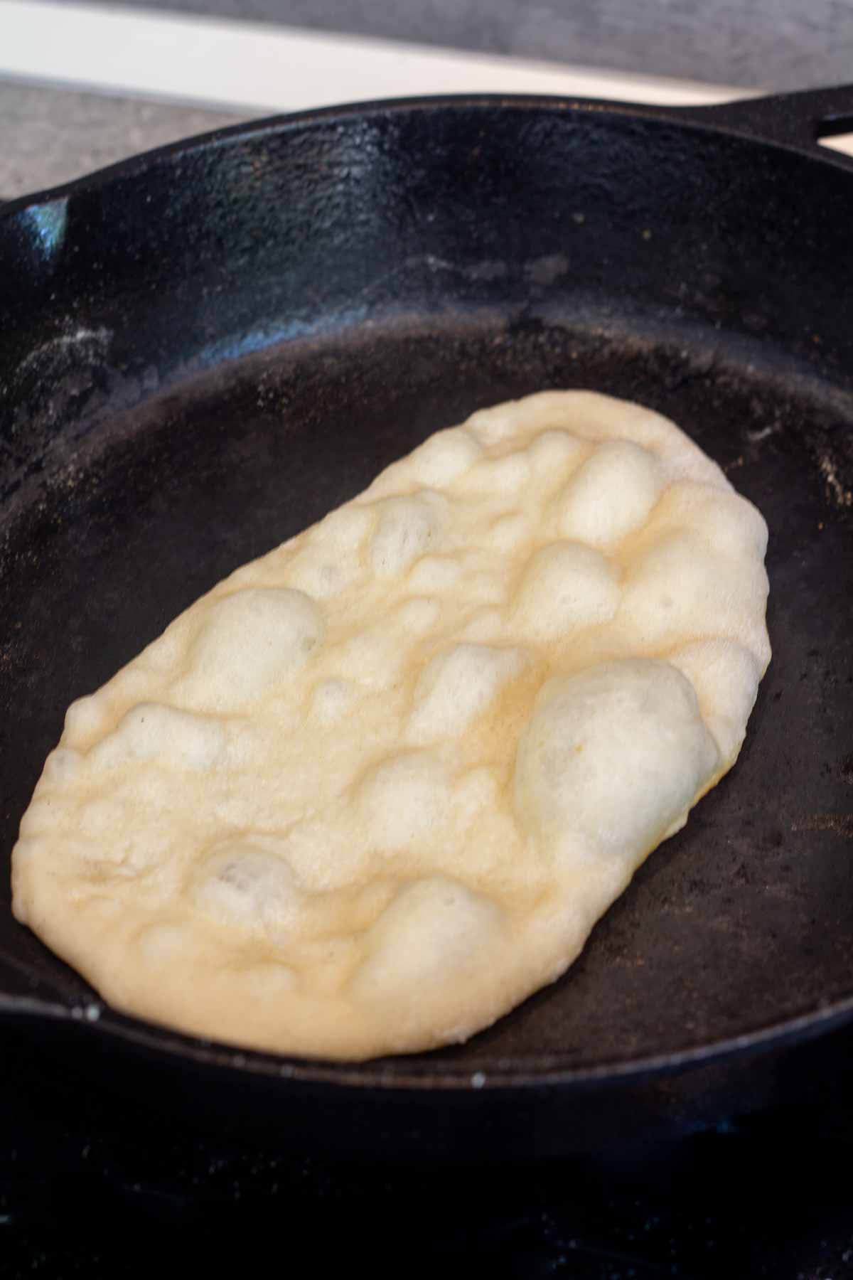 Cooking bubbly naan on a hot cast-iron skillet.