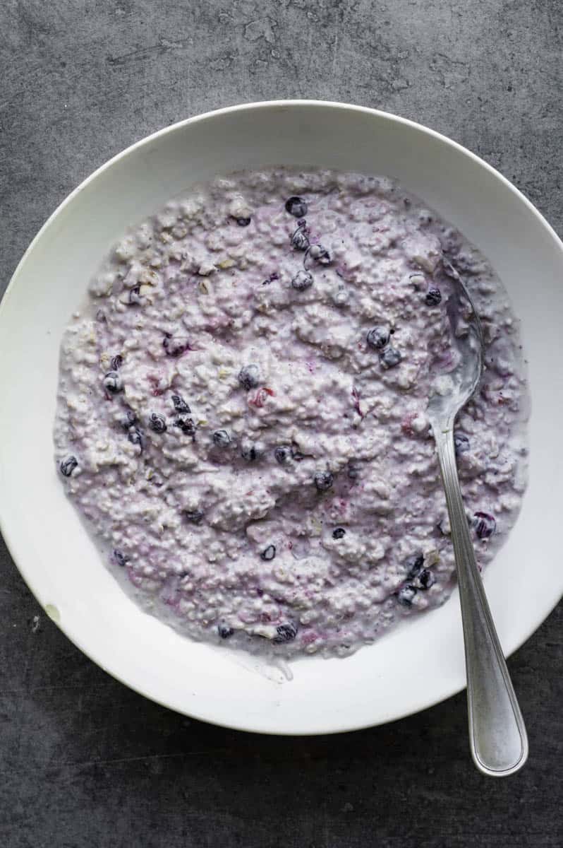 Soaked overnight oats in a white bowl with a silver spoon in it.