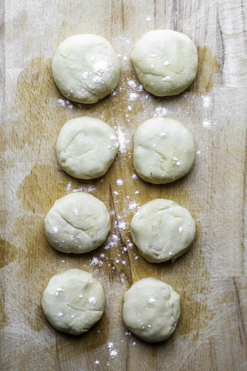 Eight small dough balls resting in a wooden cutting board.