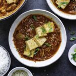 A white bowl filled with vegetarian kimchi jjigae and topped with green onion and sesame seeds.