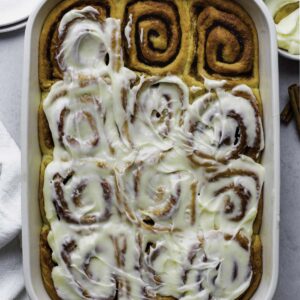 Cinnamon rolls in a ceramic baking dish topped with cream cheese frosting.