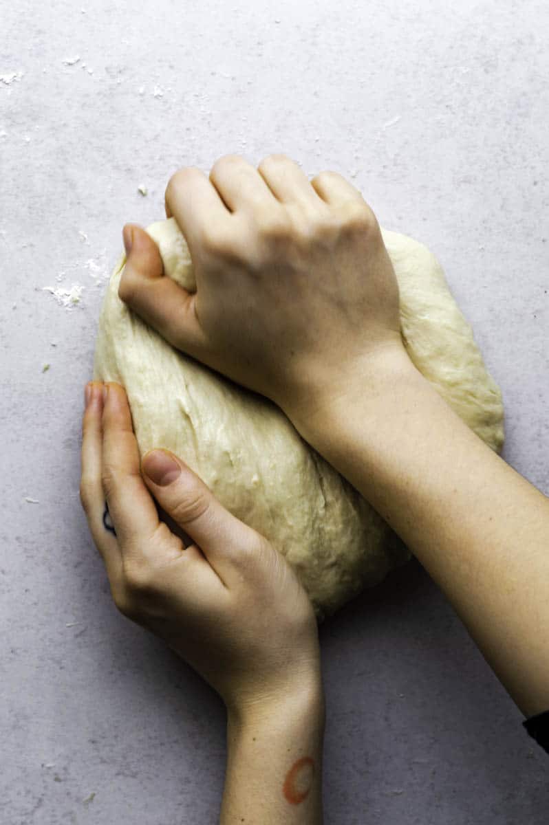 Two hands kneading dough on a countertop.