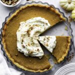 Pumpkin pie without evaporated milk in a glass pie tin topped with whipped cream and crushed pecans.