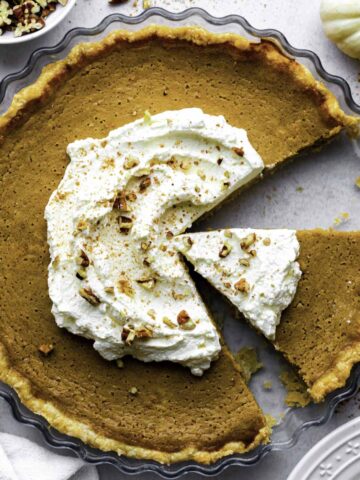 Pumpkin pie without evaporated milk in a glass pie tin topped with whipped cream and crushed pecans.
