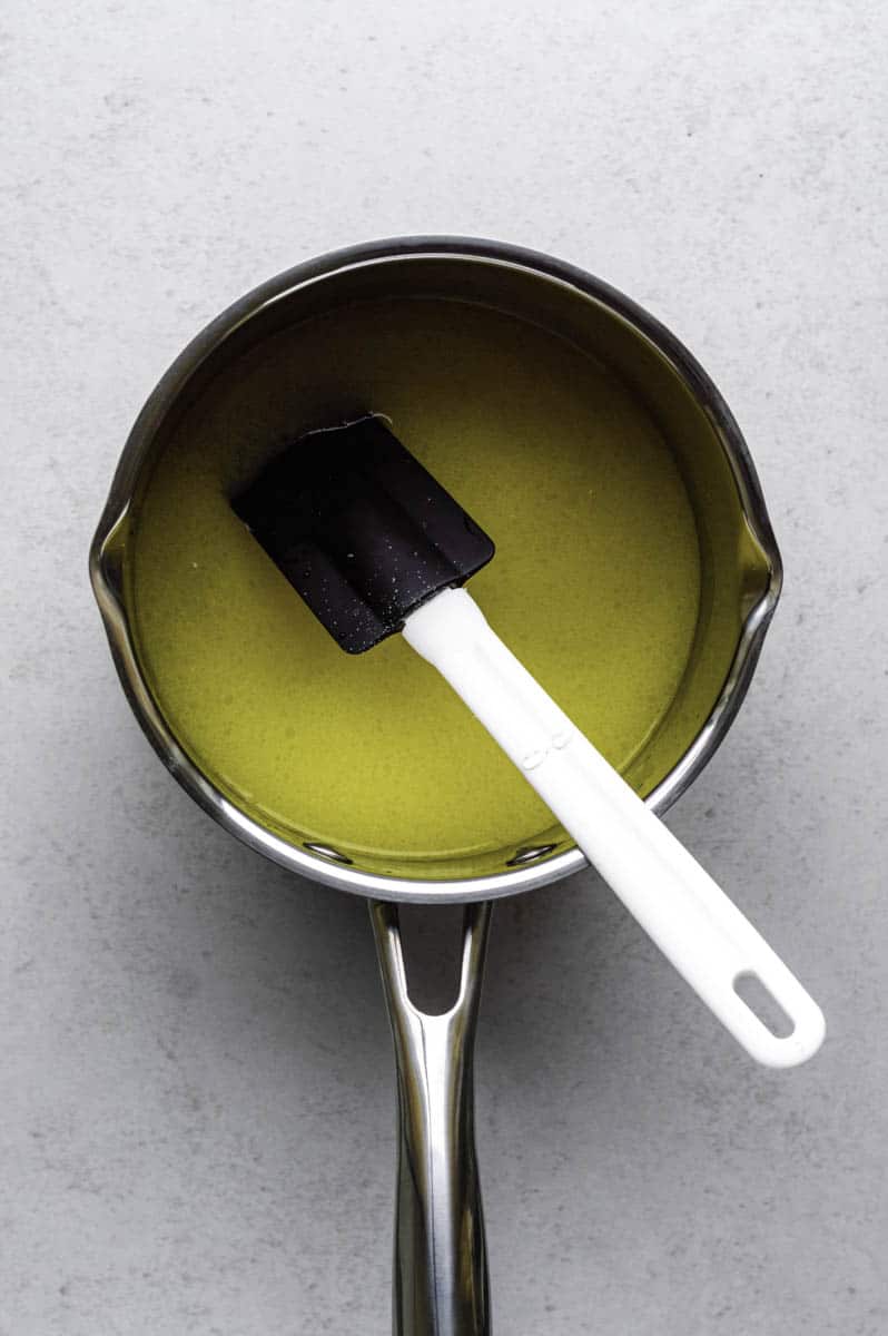 A mixture of butter, water, and sugar in a stainless-steel saucepan with a rubber spatula in it.
