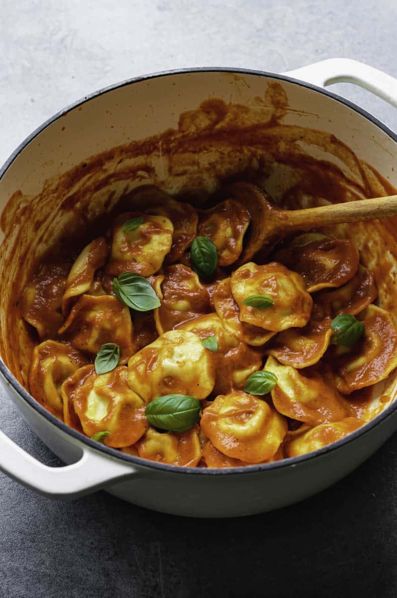 Vegan pasta Pomodoro topped with fresh basil leaves in a white Dutch Oven.