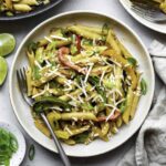 Vegetarian rasta pasta served in a creme bowl and topped with vegan cheese shreds and chopped green onion.