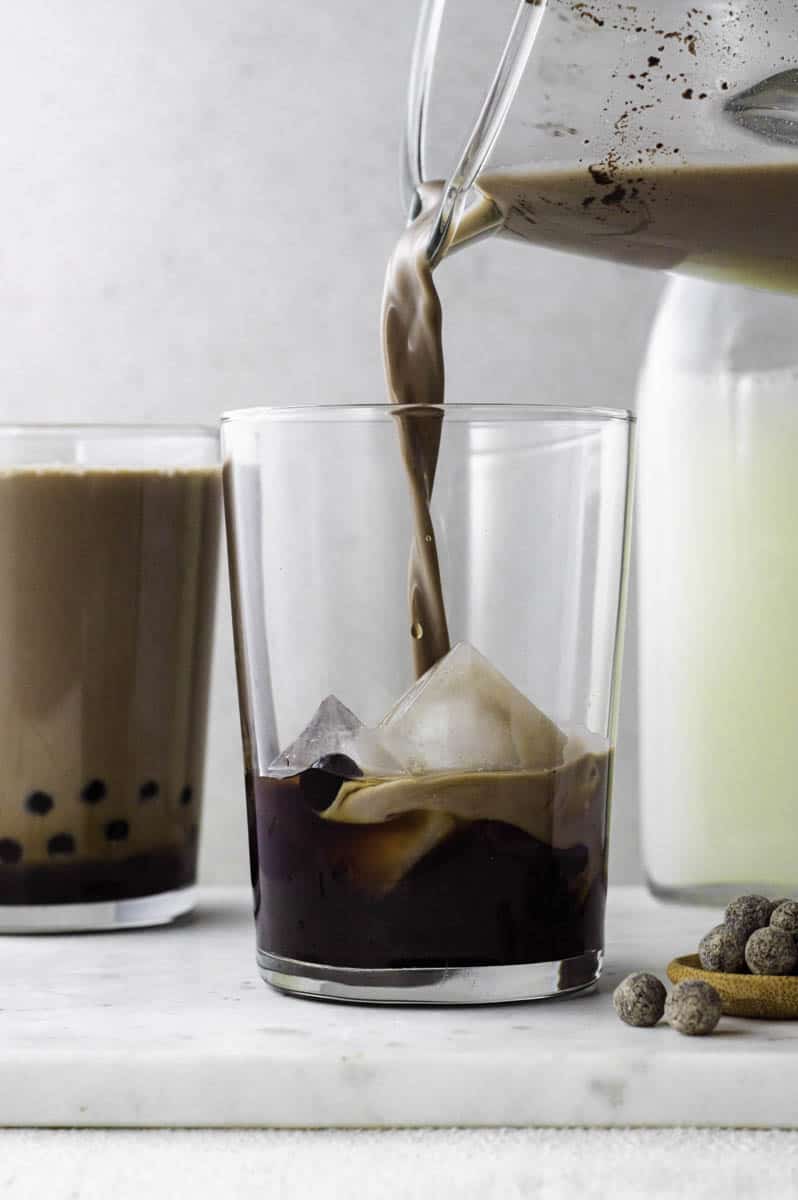 Pouring Oreo milk tea into a large glass filled with tapioca pearls and ice cubes.