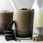 Oreo bubble milk tea served in a large glass with a boba straw in it. Four Oreo cookies placed next to the glass.