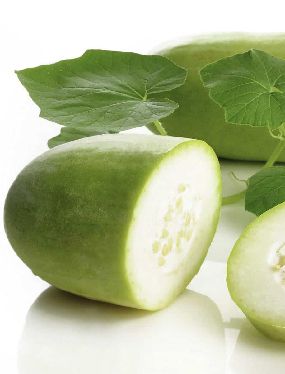 A halved winter melon on a white background with a snob of green leaves behind it,