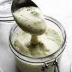 A spoon dipping in a glass jar filled with oat milk bechamel.