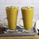 Two glasses filled with carrot banana smoothie and topped with chopped cashew nuts.