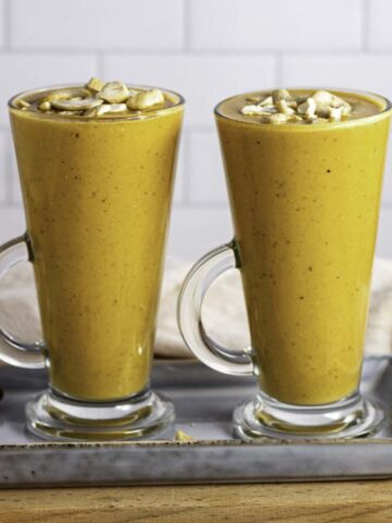 Two glasses filled with carrot banana smoothie and topped with chopped cashew nuts.