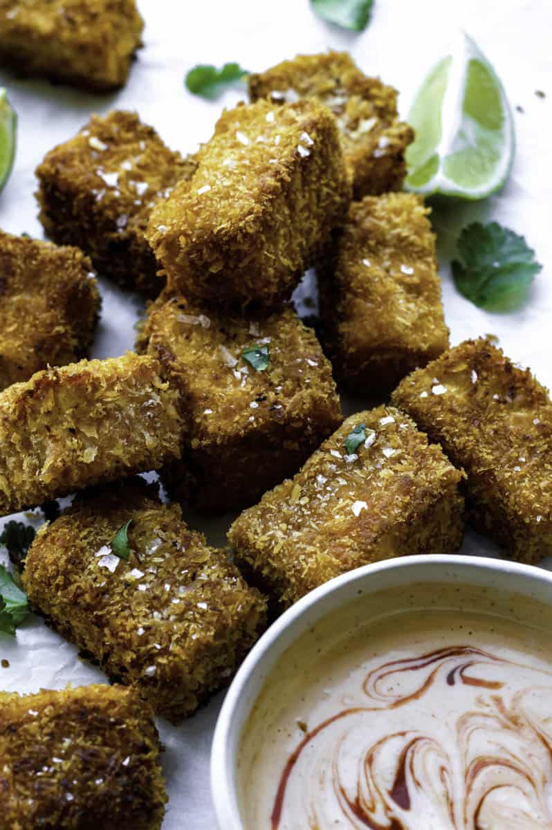 Fried silken tofu cubes placed next to a small bowl filled with sauce.