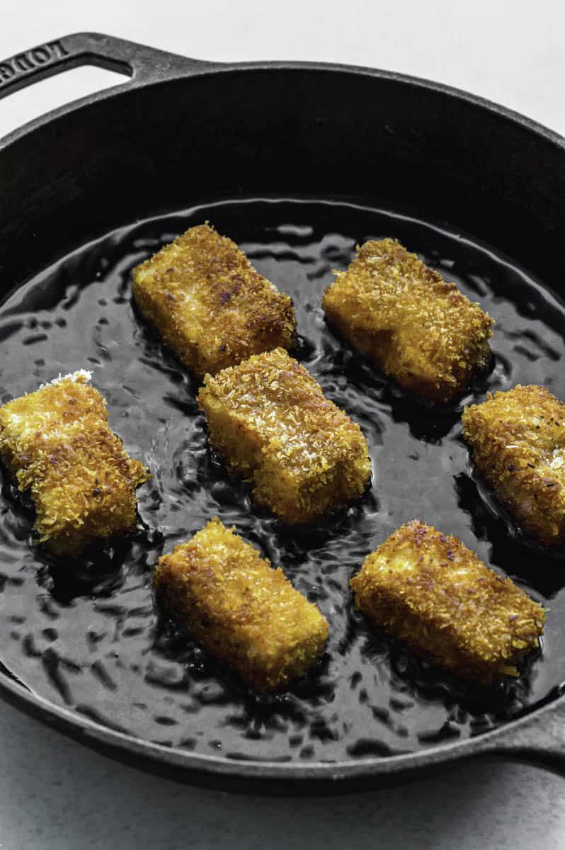 Tofu pieces frying in a cast-iron skillet.