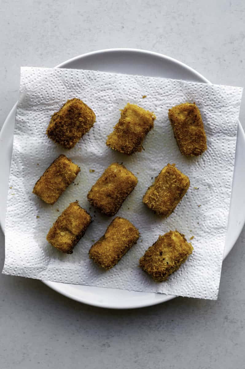 Fried tofu pieces resting on a plate layered with a paper towel.