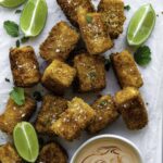 Fried silken tofu cubes served on a piece of parchment paper, and topped with sea salt and fresh cilantro.