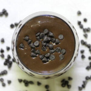 A glass filled with chocolate smoothie and topped with chocolate chips.