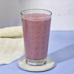 Blueberry smoothie in a lagre glass jar on a blue table.