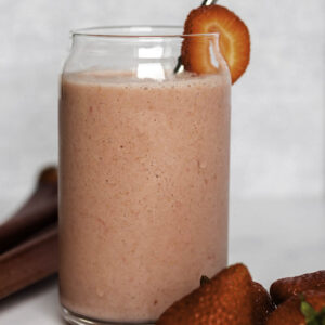 A glass with a smoothie and piles of fresh strawberries next to it.