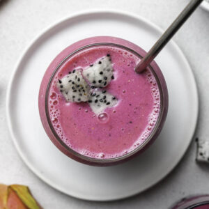 Dragon fruit strawberry smoothie in a glass with a straw and topped with pieces of dragon fruit.