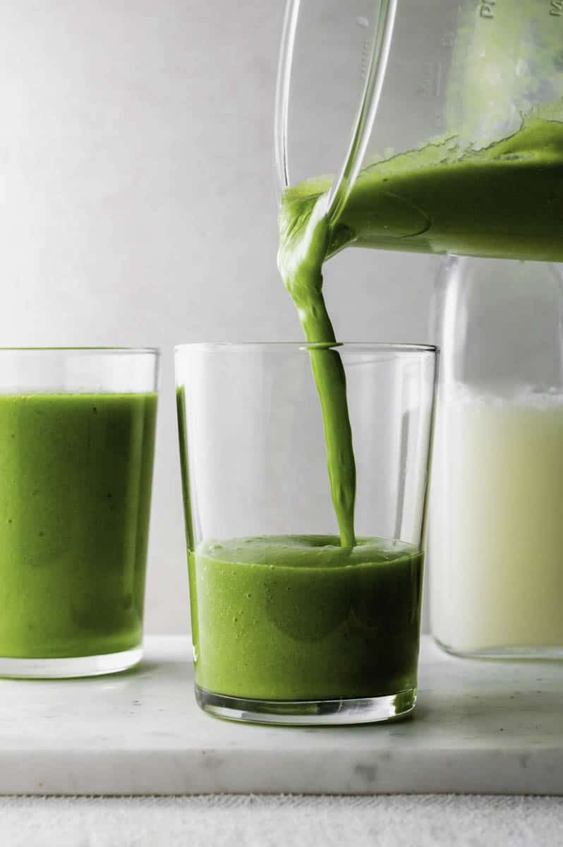 Pouring green smoothie from a blender to a glass cup.